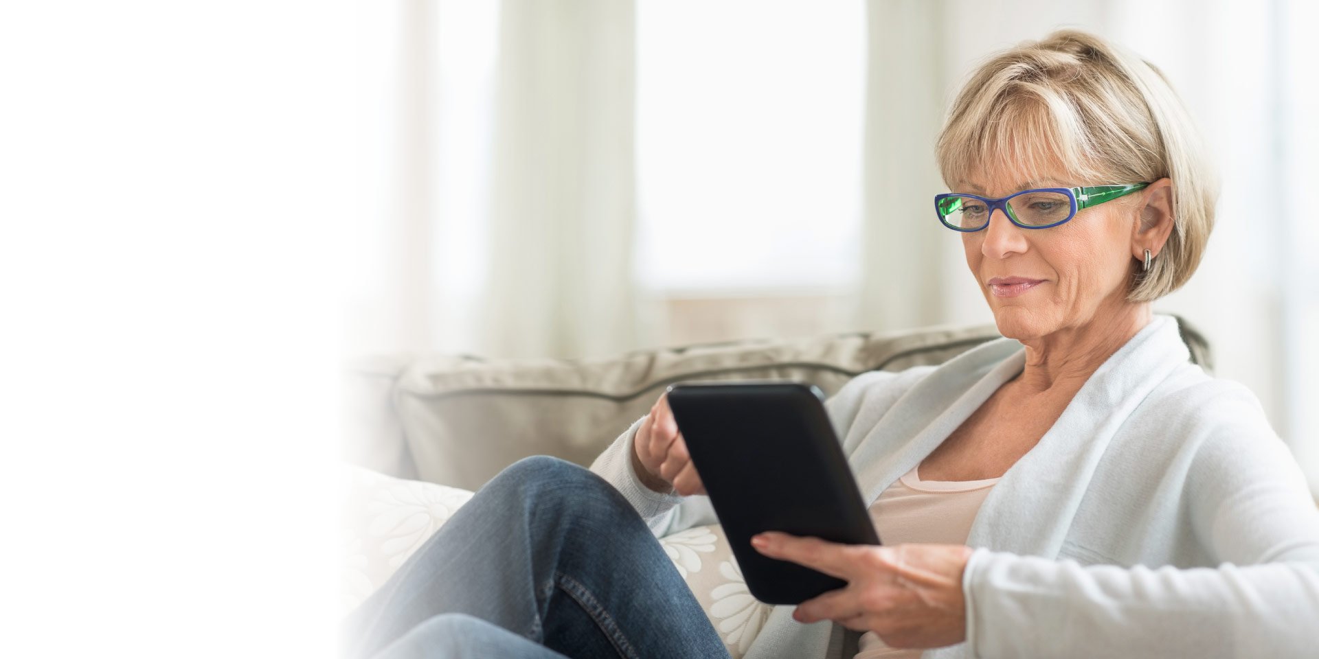 Woman sitting on her couch looking at Old National's checking offer on a tablet