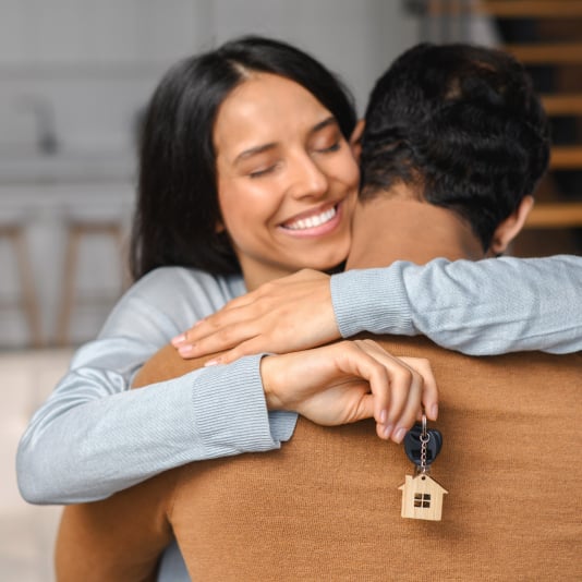 Young couple hugs as they hold keys to their new home