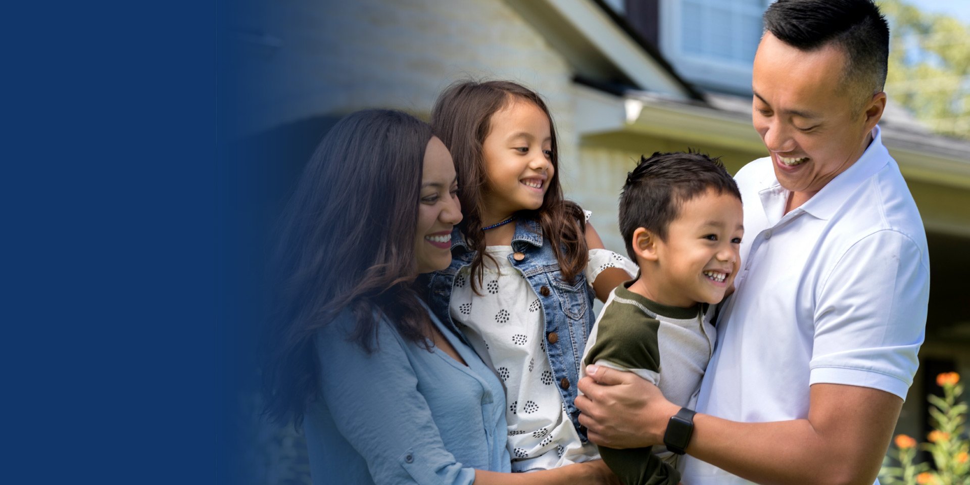 A young family hugs in the front yard of their new home